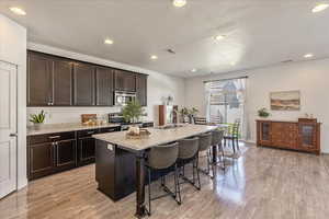 Kitchen with dark wood finish cabinetry, a center island with sink, a breakfast bar area, light wood-style flooring, and stainless steel appliances