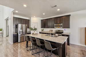 Kitchen featuring dark wood finish cabinets, stainless steel appliances, a center island with sink, a breakfast bar, and a textured ceiling