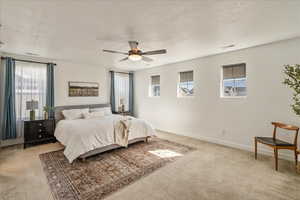 Bedroom with light colored carpet, multiple windows, a textured ceiling, and ceiling fan