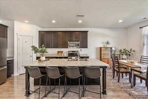 Kitchen featuring dark wood finish cabinetry, a breakfast bar area, a center island with sink, light wood-style flooring, and stainless steel appliances