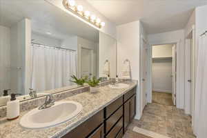 Full bath with double vanity, a shower with curtain, stone finish flooring, and a walk in closet