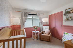 Bedroom featuring wainscoting, a crib, light carpet, and a closet