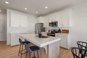 Kitchen featuring stainless steel appliances, a center island with sink, a kitchen breakfast bar, white cabinets, and light wood finished floors