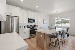 Two tone kitchen with stainless steel appliances, a center island with sink, two tone color scheme, light wood finished floors, and a breakfast bar area
