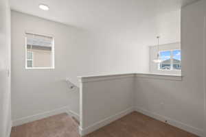 Hallway with an upstairs landing and light colored carpet