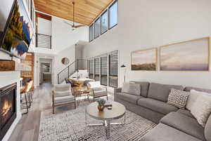 Living area with a glass covered fireplace, light wood-type flooring, ceiling fan, and a high wooden ceiling