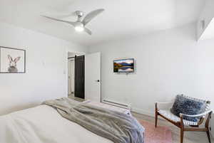 Bedroom with baseboard heating, light wood-style flooring, and ceiling fan