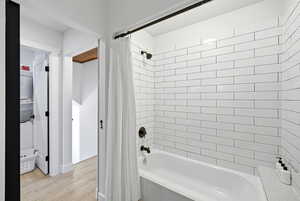 Full bath with shower / bath combo with shower curtain and light wood-style floors
