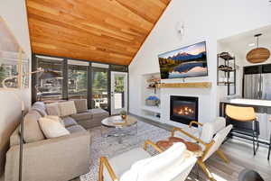 Living room featuring wood finished floors, a glass covered fireplace, and a vaulted wood ceiling