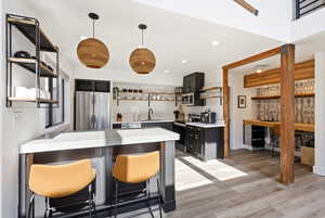 Kitchen with open shelves, a kitchen bar, a peninsula, stainless steel appliances, and light wood-style floors