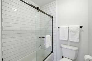 Full bathroom featuring toilet and shower / bath combination with glass door