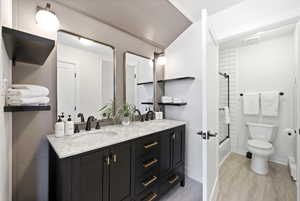 Bathroom with double vanity, shower / bathtub combination, light wood-type flooring, and baseboard heating