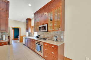 Kitchen with stainless steel appliances, wood finish cabinets, glass insert cabinets, backsplash, and light stone counters