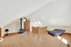 Bonus room with light wood finished floors, a skylight, a wood stove, and vaulted ceiling