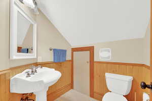 Half bathroom with a wainscoted wall, vaulted ceiling, and wood walls