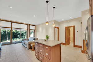 Kitchen featuring a kitchen island, wood finish cabinetry, freestanding refrigerator, hanging light fixtures, and open floor plan
