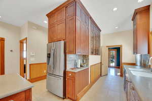 Kitchen with wainscoting, stainless steel fridge with ice dispenser, glass insert cabinets, wooden walls, and light tile patterned flooring
