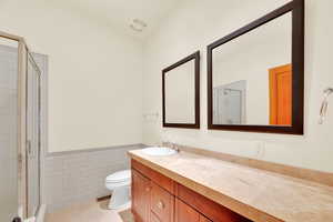 Bathroom featuring tile walls, a wainscoted wall, a stall shower, vanity, and light tile patterned floors