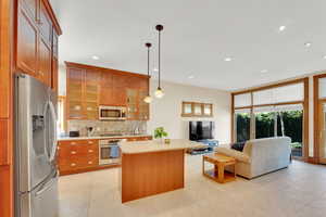 Kitchen featuring stainless steel appliances, light countertops, a kitchen island, wood finish cabinets, and glass insert cabinets