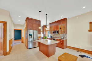 Kitchen featuring stainless steel appliances, glass fronted cabinets, wood finish cabinets, and decorative light fixtures