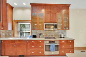 Kitchen featuring stainless steel appliances, backsplash, wood finish cabinets, recessed lighting, and glass insert cabinets