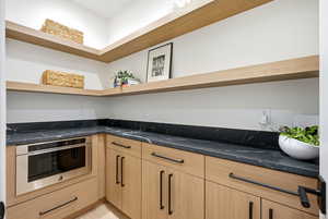 Kitchen featuring oven, light wood finish cabinets, dark stone counters, open shelves, and modern cabinets