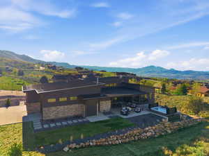 Rear view of property featuring a mountain view, a yard, a patio, a standing seam roof, and stone siding