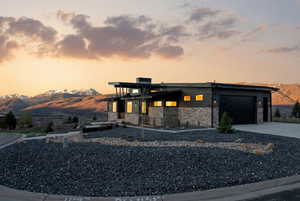 Contemporary home featuring a mountain view, stone siding, a garage, driveway, and a chimney