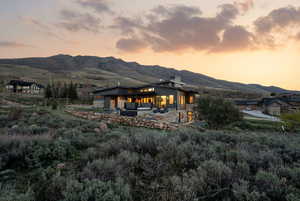 Back of property at dusk featuring a patio, a mountain view, and stone siding