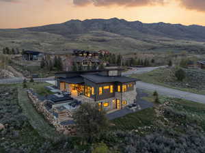 Back of property at dusk featuring stone siding, a standing seam roof, a patio, a mountain view, and a yard
