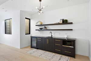 Indoor wet bar featuring modern cabinets, beverage cooler, open shelves, light wood finished floors, and black microwave