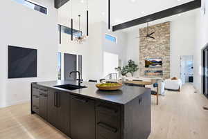 Kitchen featuring an island with sink, a high ceiling, modern cabinets, a stone fireplace, and light wood-type flooring