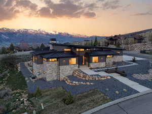 Contemporary house featuring stone siding, a standing seam roof, a mountain view, and a chimney
