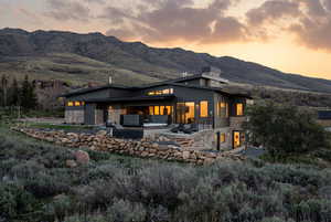 Back of house at dusk with stone siding, a patio, a mountain view, and a chimney