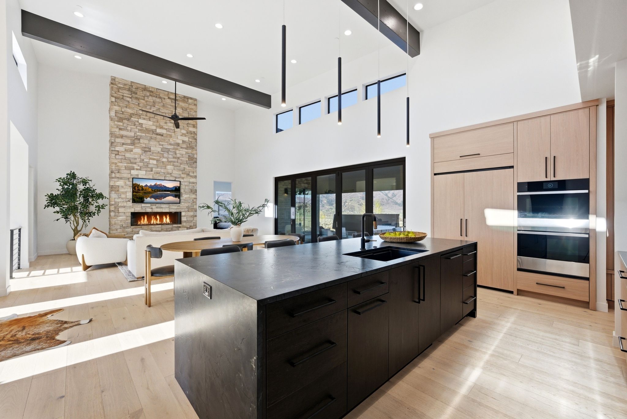 Kitchen featuring a large island with sink, a stone fireplace, light wood-type flooring, stainless steel double oven, and modern cabinets