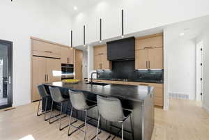 Kitchen with modern cabinets, a breakfast bar, light wood finish cabinetry, a high ceiling, and recessed lighting