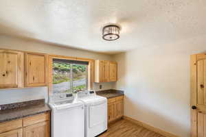 Laundry room with light wood-style floors, washing machine and clothes dryer, cabinet space, and a textured ceiling