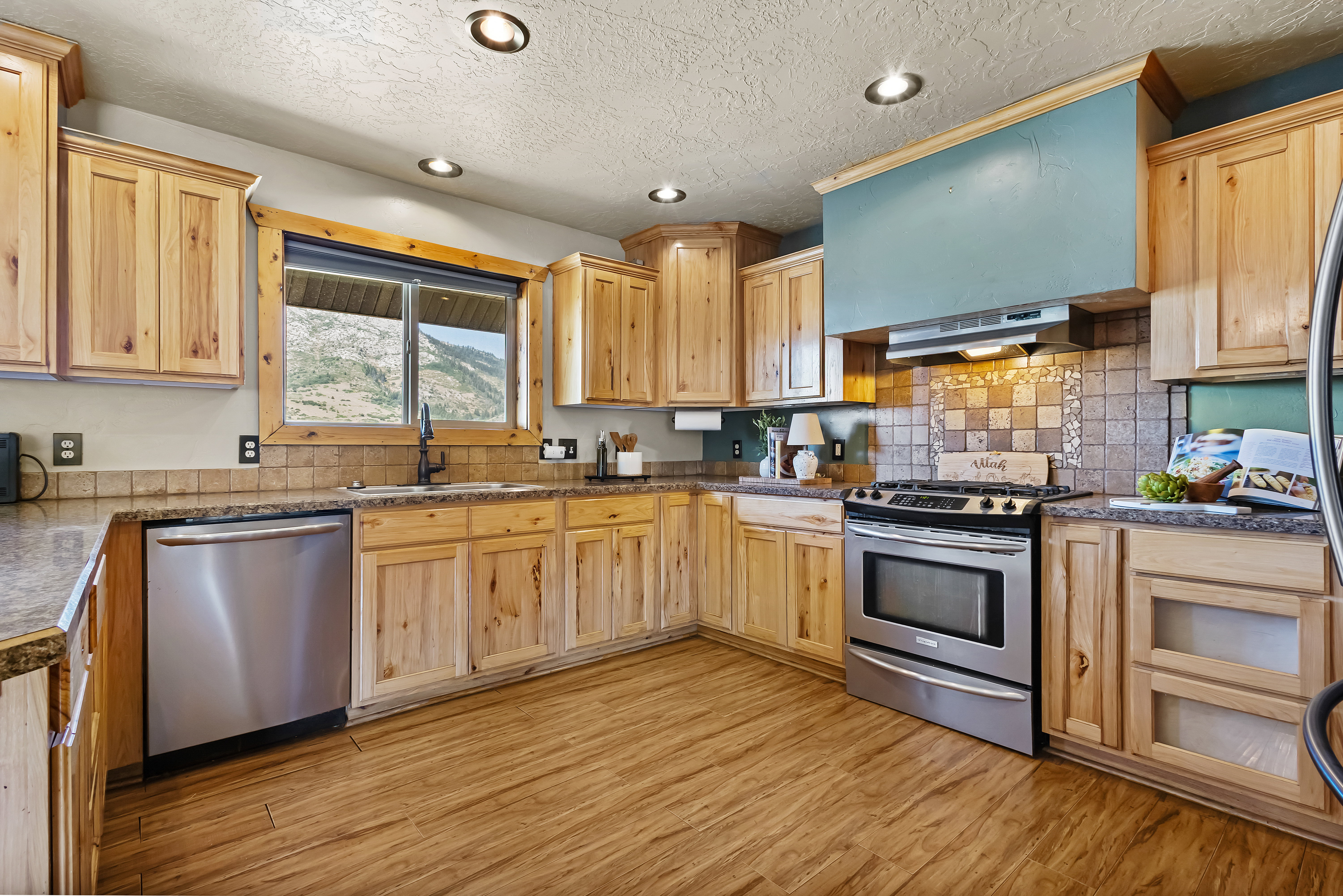 Kitchen with stainless steel appliances, recessed lighting, light wood finish cabinetry, light wood-type flooring, and a textured ceiling