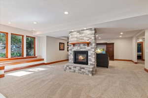Unfurnished living room with light colored carpet, a stone fireplace, and recessed lighting