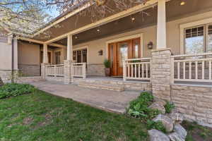 Doorway to property with stone siding, stucco siding, and a porch