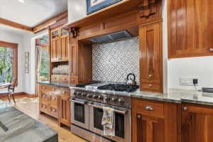 Kitchen featuring range with two ovens, light stone countertops, wood finish cabinetry, tasteful backsplash, and light wood-style flooring