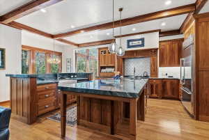 Kitchen with beamed ceiling, dark stone counters, light wood-type flooring, wood finish cabinets, and tasteful backsplash