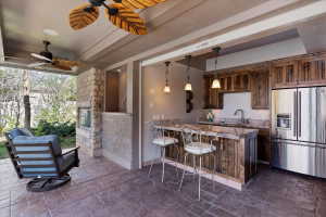 Kitchen featuring stainless steel fridge, stone tile flooring, a peninsula, dark wood finish cabinetry, and a kitchen breakfast bar