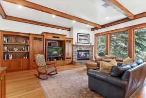 Living room with beam ceiling, a stone fireplace, light wood-style flooring, and recessed lighting