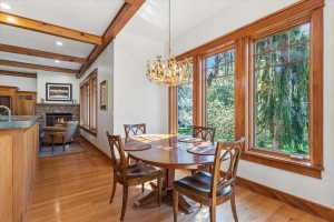 Dining space with beamed ceiling, hanging lights, a stone fireplace, and light wood finished floors