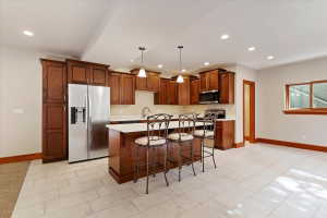 Kitchen featuring a breakfast bar, stainless steel appliances, light countertops, hanging light fixtures, and a center island with sink