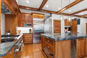 Kitchen with built in appliances, wood finish cabinetry, a large island with sink, a warming drawer, and beamed ceiling