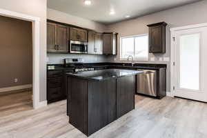 Kitchen featuring dark wood finish cabinets, stainless steel appliances, light wood-style floors, a kitchen island, and dark stone countertops