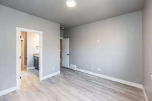 Unfurnished bedroom featuring ensuite bath and light wood-style flooring