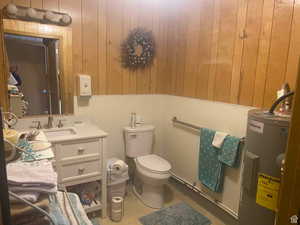 Half bathroom with vanity, water heater, and wood walls
